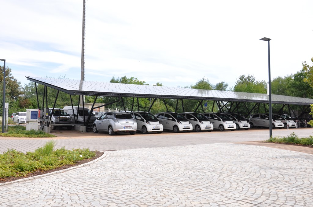 Großer Solar-Carport mit Photovoltaikmodulen, unter dem mehrere Elektrofahrzeuge parken und aufgeladen werden.