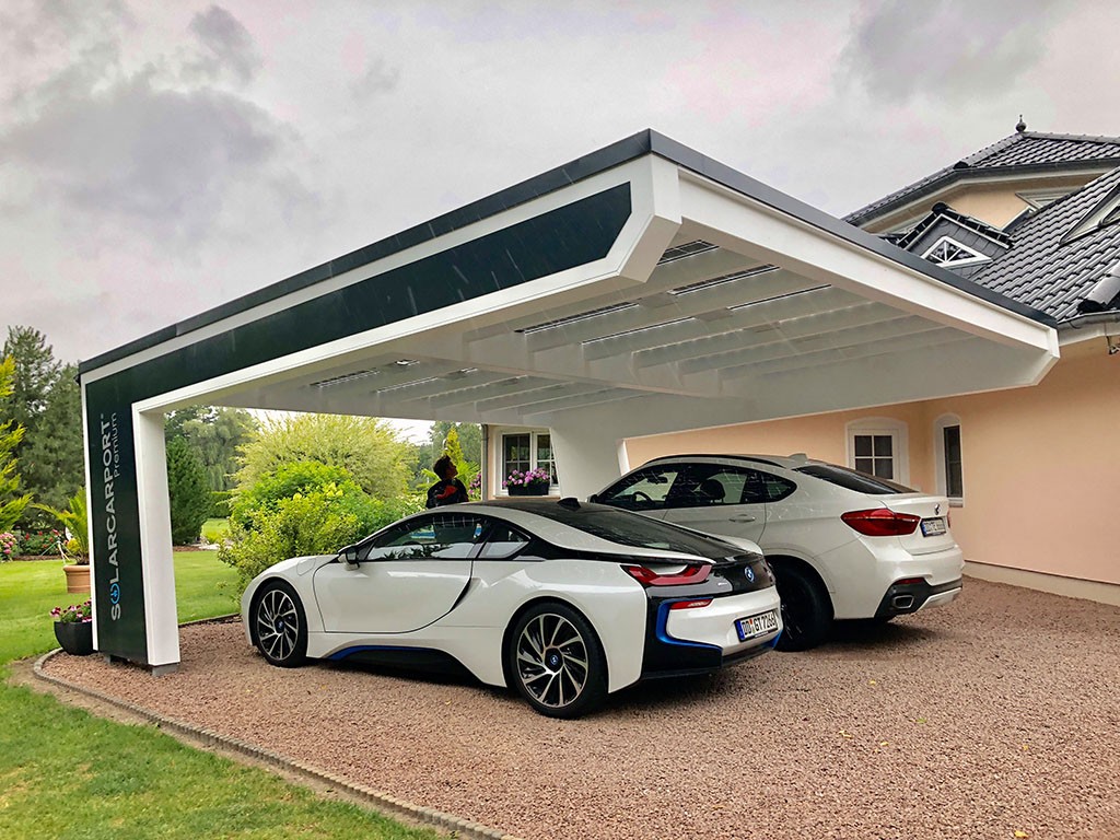 Ein moderner Solar-Carport mit Photovoltaikmodulen, unter dem zwei Fahrzeuge geparkt sind, neben einem eleganten Einfamilienhaus.